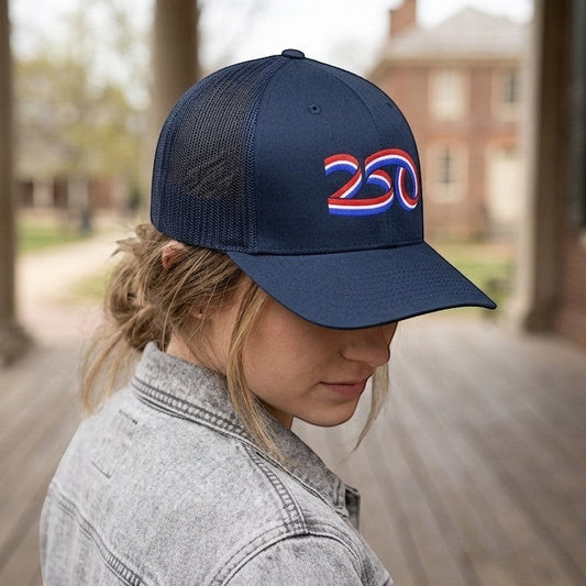 Americana navy blue trucker hat with a red, white, and blue 250 ribbon graphic, worn by a woman outdoors.
