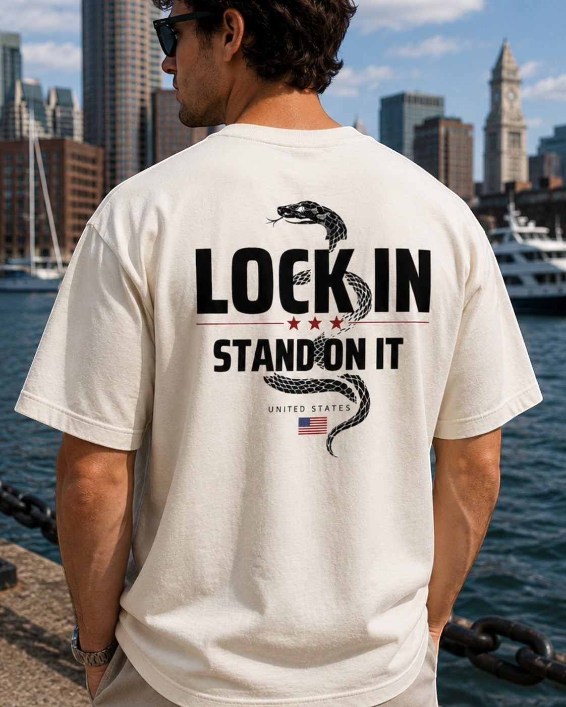 Americana off-white crewneck t-shirt with a back graphic of a coiled snake and the slogan LOCK IN STAND ON IT.