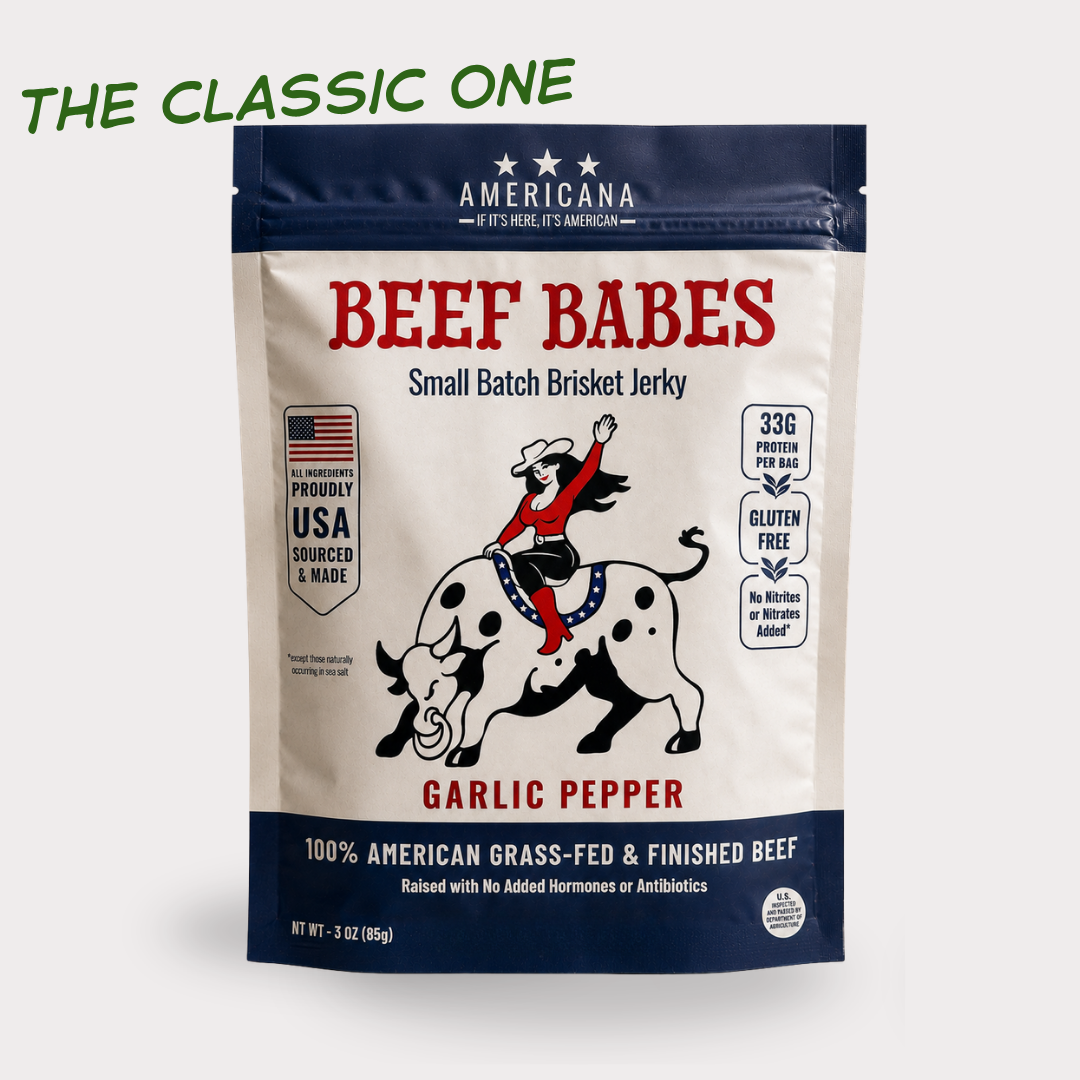 A stand-up pouch of Americana Beef Babes Garlic Pepper Jerky on a light gray background. The package is cream and navy blue with red text and an illustration of a cowboy riding a black-and-white spotted bull.