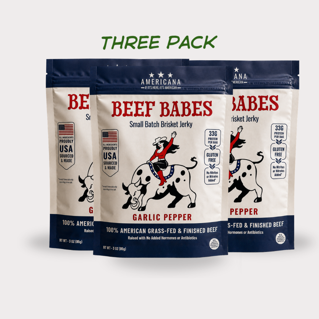 Three stand-up pouches of Americana Beef Babes Small Batch Brisket Jerky in Garlic Pepper flavor, arranged as a three-pack on a light gray background with green text reading 'THREE PACK' above them.