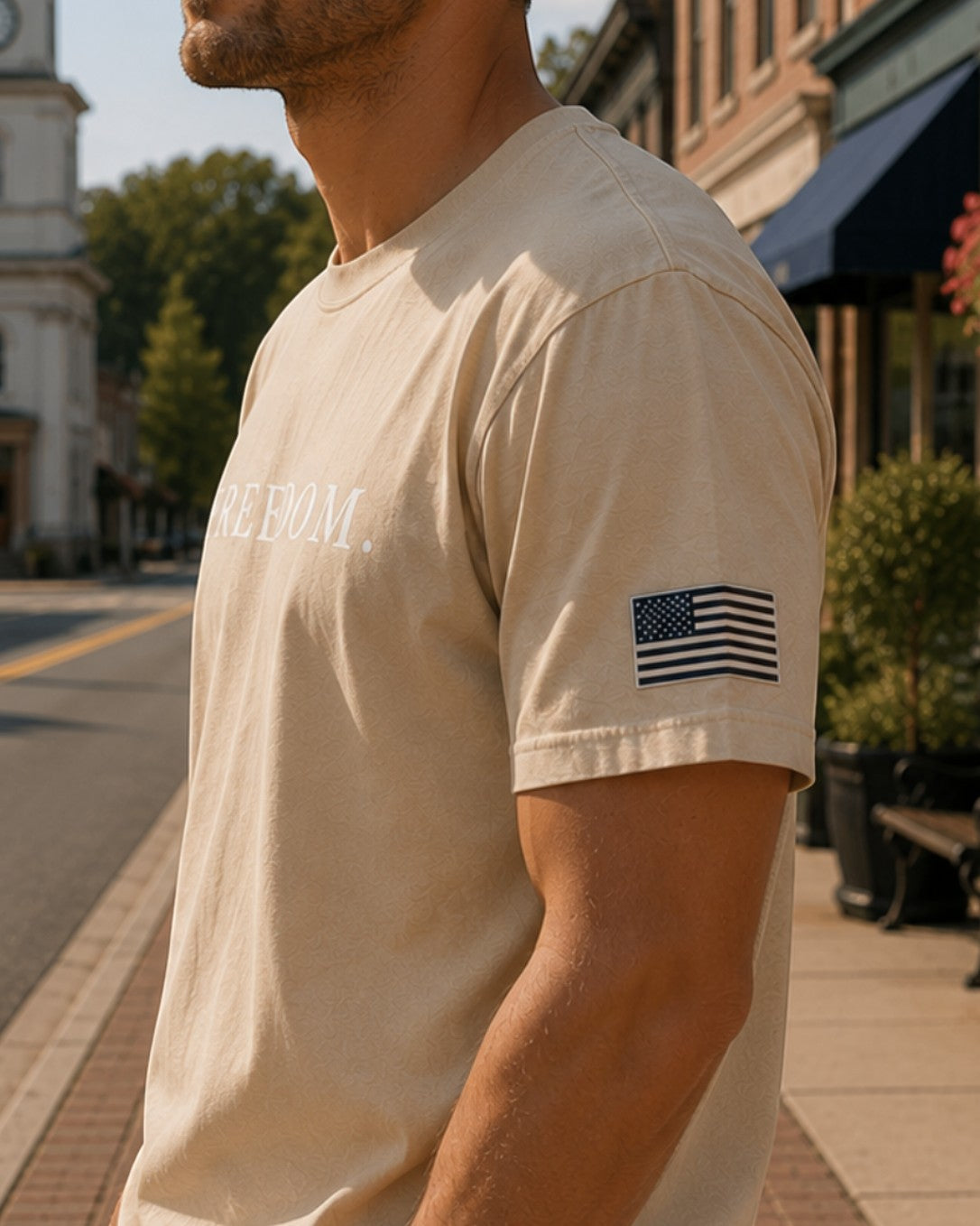 Americana AM Freedom beige cotton chore tee with American flag sleeve patch worn by a man on a city street