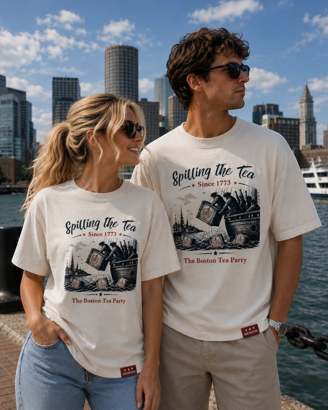Americana off-white cotton crewneck t-shirts featuring a Boston Tea Party graphic, worn by a couple in a city harbor.