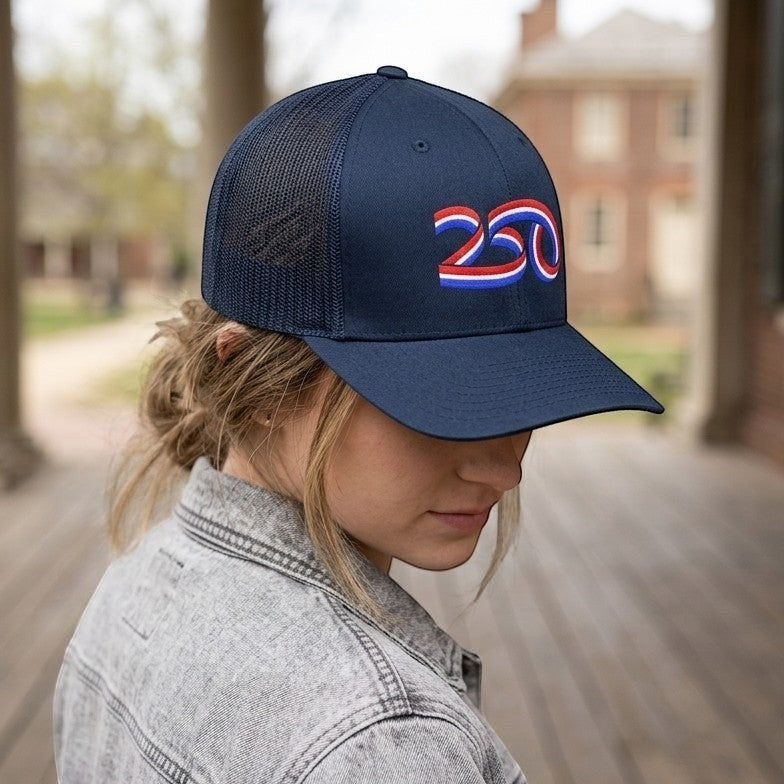 Americana navy blue trucker hat with a red, white, and blue 250 ribbon graphic, worn by a woman outdoors.